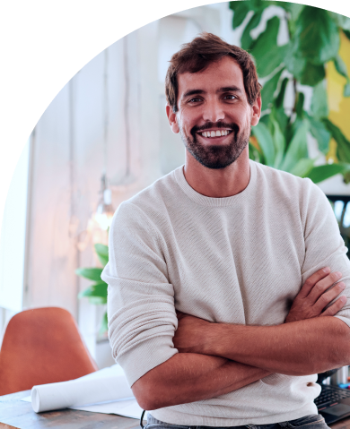 Young male designer smiling while leaning on a table in an office with his arms crossed